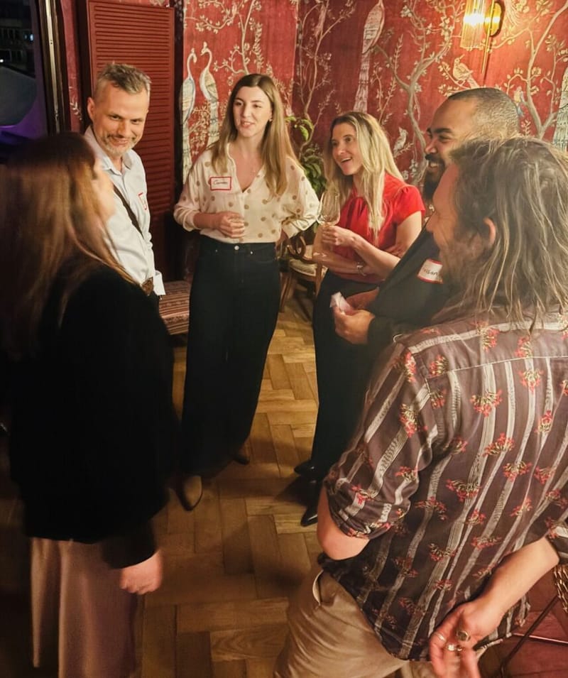 Small group of guests with name tags in conversation at a cocktail party venue with ornate red floral wallpaper