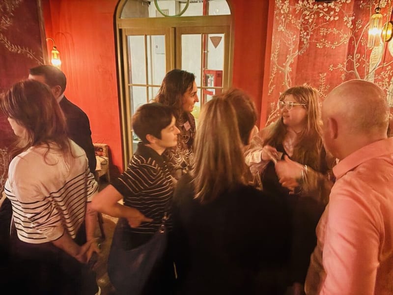 Guests mingling in animated conversation at a cocktail party, ornate red wallpaper in the background