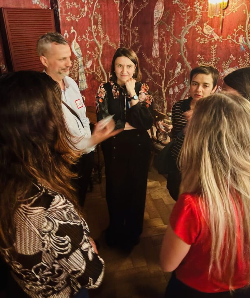 Small circle of guests listening attentively during a conversation at a cocktail party, red wallpaper in the background