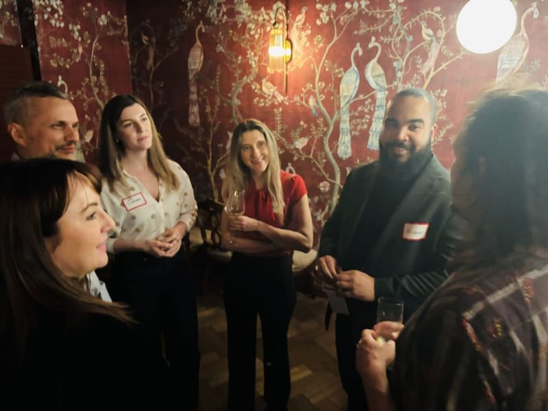Small group of guests chatting and holding drinks at a 3rd Space Bucharest event, with ornate red wallpaper in the background