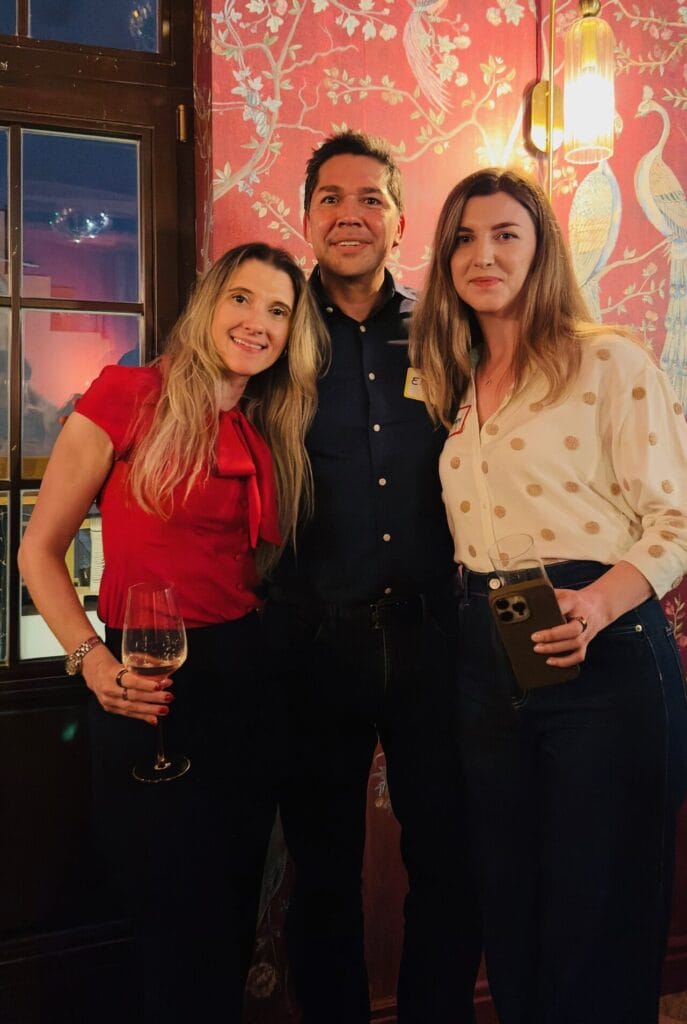 Eric Melchor wearing a name tag posing with two women at a cocktail party, one holding a glass of wine