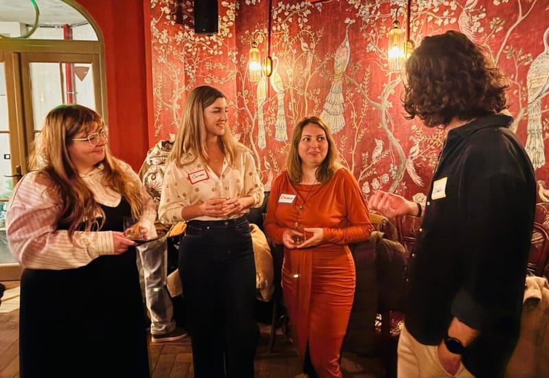 Four guests chatting in a small circle at a cocktail party, red bird-and-branch wallpaper behind them