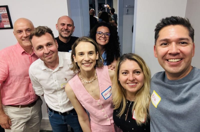 Eric Melchor and six guests wearing name tags smiling together at a Bucharest cocktail party