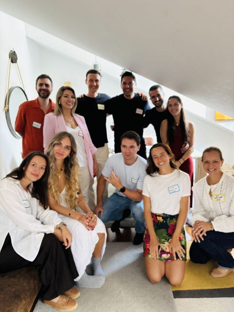 Group of about ten people wearing name tags posing together on a staircase landing inside a bright modern Lisbon apartment