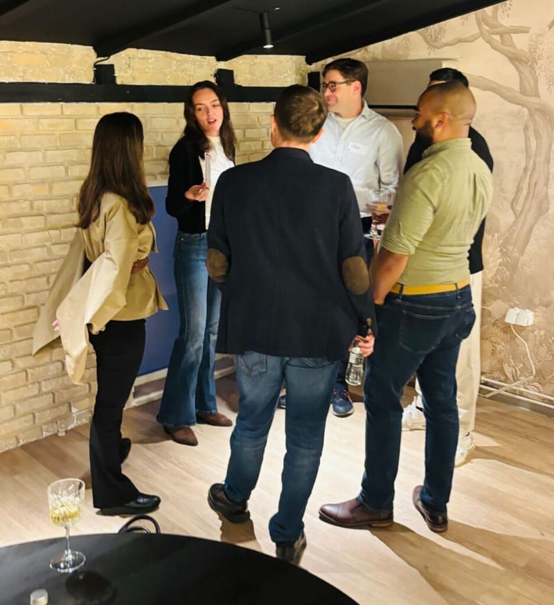 Group of five people in conversation at a 3rd Space Bucharest networking event, standing against a stone brick wall with a nature mural